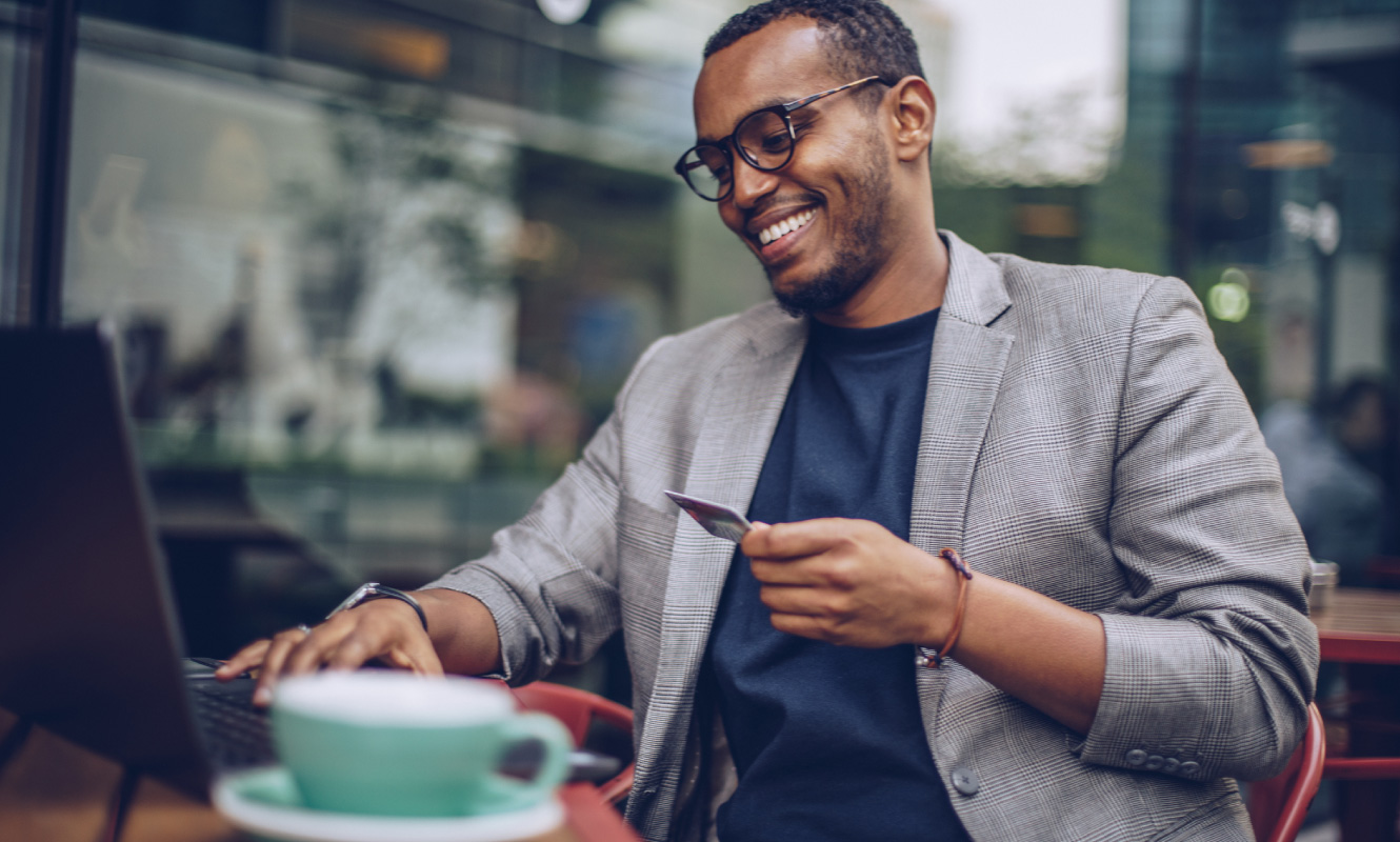 Man smiling and looking at a laptop. He is holding a credit card in one hand and typing.