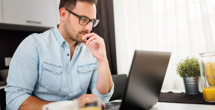 Man with glasses looking intently at a black laptop. 