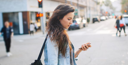 Young woman crossing an intersection while looking down at her phone.