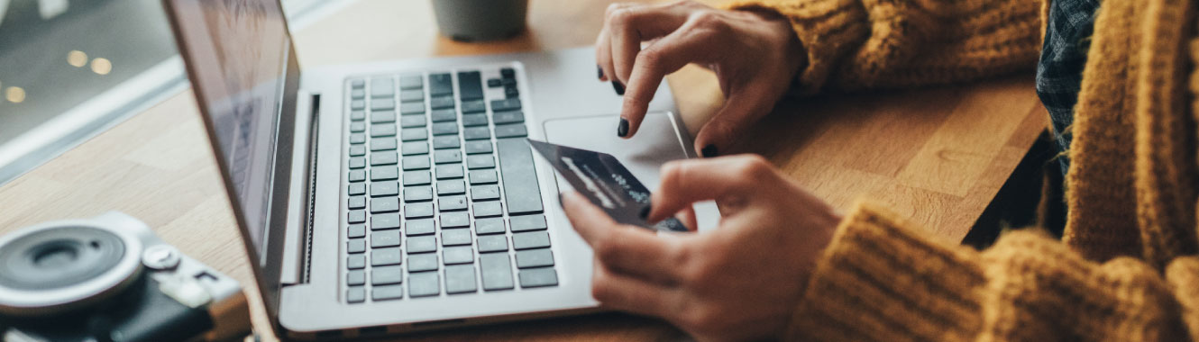 Close up of a woman's hands. One hand is holding a credit card while the other is using a laptop. 