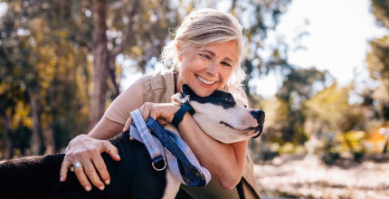 A woman hugging a black and white dog outside.