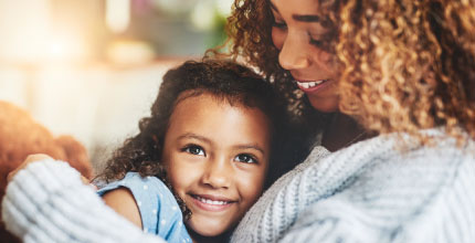 A young girl being held by her mom. They are both smiling. 