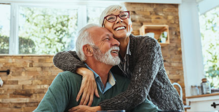 A senior couple in a modern kitchen embracing and smiling. 