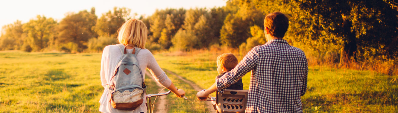 A young family pushing bikes in a field. 