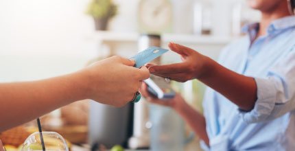 Close up of a person's hands giving a credit card to another person holding a card machine. 