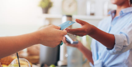 Close up of a person's hands giving a credit card to another person holding a card machine.