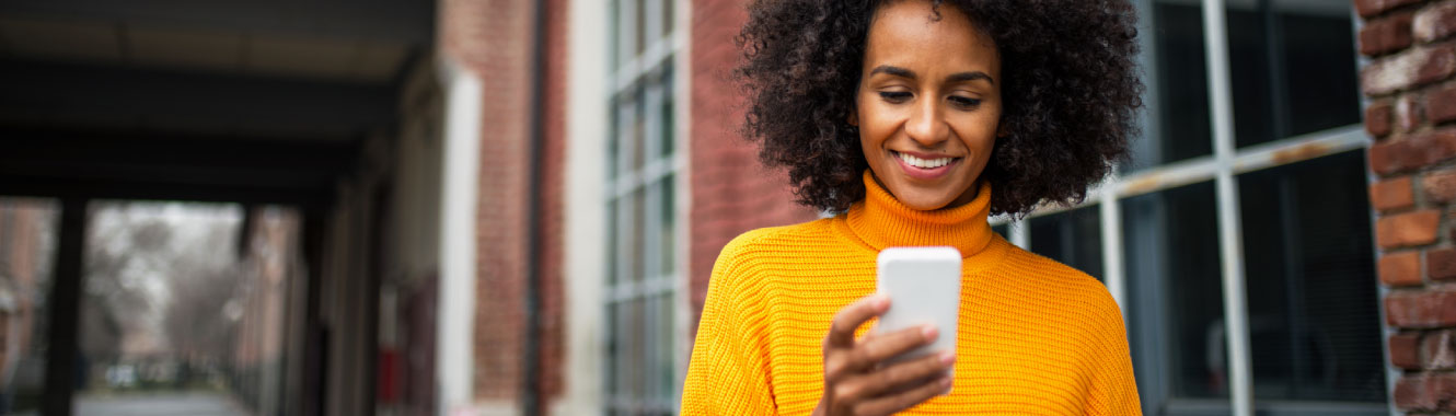 Woman in yellow sweater looking at a cell phone. 