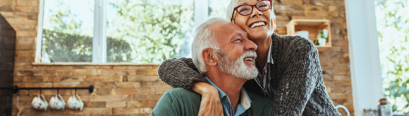 A mature couple smiling and hugging in a kitchen. 