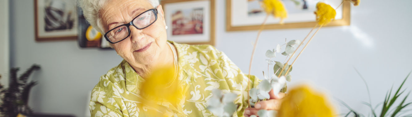 A senior woman tending to flowers in her home. 